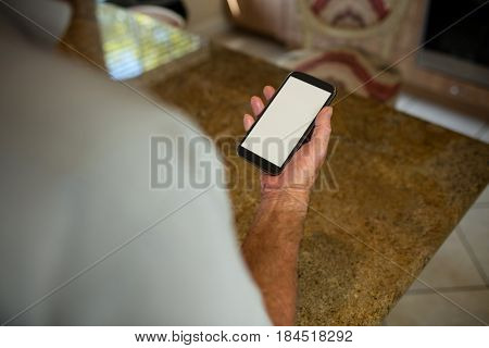 Mid-section of senior man holding mobile phone in the ktchen at home