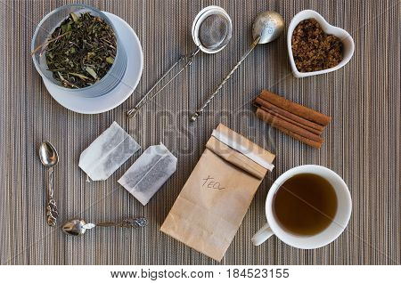 Teatime flat lay. Loose leaf tea in crystal jar tea bags cup of hot tea brown sugar and cinnamon infuser and vintage spoons View from above.