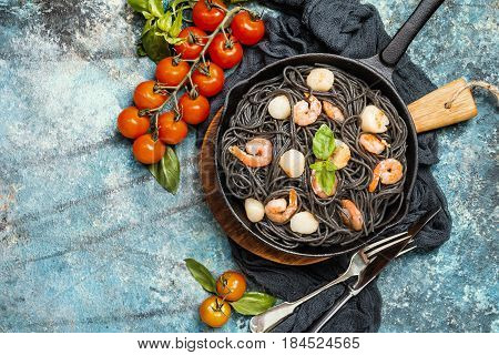 Black spaghetti with prawns and scallop in frying pan on blue background, top view with copy space