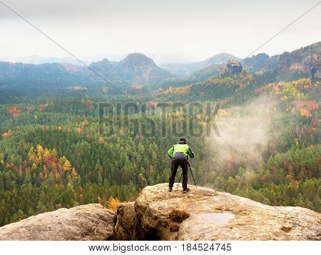 Hiker With Camera On Tripod Takes Picture From Rocky Summit. Alone Photographer At Edge Photograph L