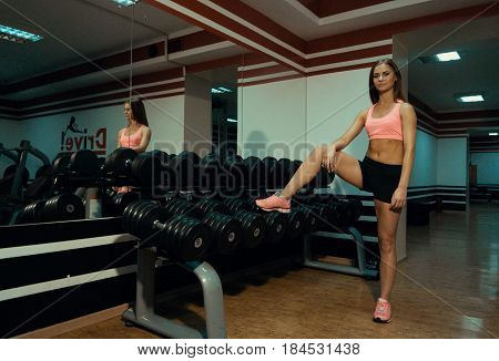 The girl put her foot on a dumbbell in the gym.