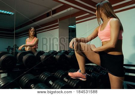 Sport girl looks in a mirror near a dumbbell in the gym.