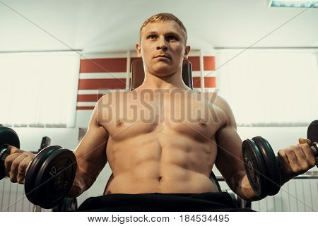 A young athlete with a bare torso doing exercises with dumbbells. Exercises for bitseps.