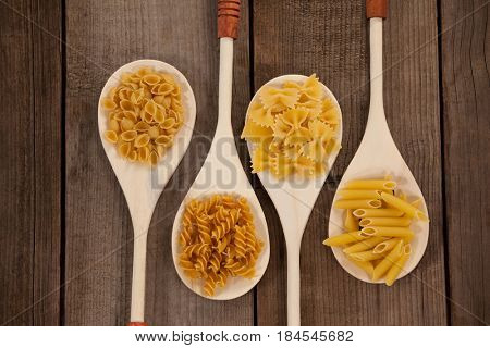 Spoons filled with varieties of pasta on wooden background