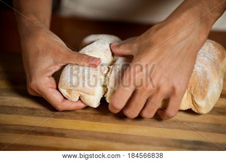 Mid section of male staff tearing a bun in bakery shop