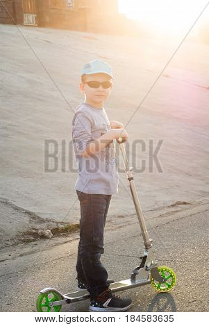 Little Boy In Sunglasses And A Cap Riding A Scooter,