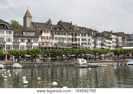 Rapperswil Switzerland - May 10 2016: Boats are moored at the marina on the shore of the Lake Zurich. There are trees that grow along the promenade and historical townhouses can be seen in distance