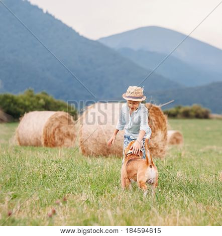 Boy plays with dog on the field with hayroll