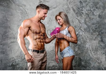 Pretty caucasian fitness girl and man on diet resting after exercise And drinking protein powder from shaker in the studion