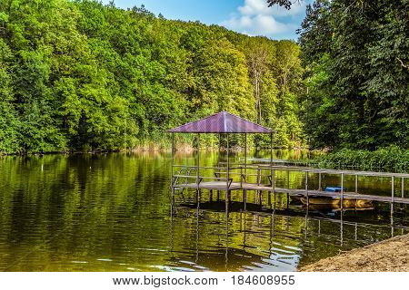 Footbridge with a gazebo and small pier for walking pedal catamaran on the lake shore. Dock for pedal boat.