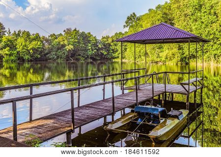 Footbridge with a gazebo and small pier for pleasure pedal catamaran on the lake shore. Dock for pedal boat and a quiet holiday in nature.