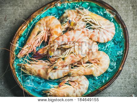 Raw uncooked tiger prawns on chipped ice in turquoise blue tray over grey concrete background, top view. Fresh seafood