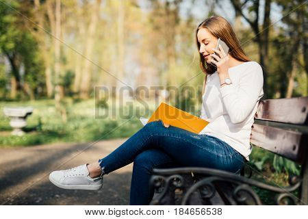 Portrait Of Attractive Young Professional Woman Using A Smartphone While Sitting On A Wooden Bench I