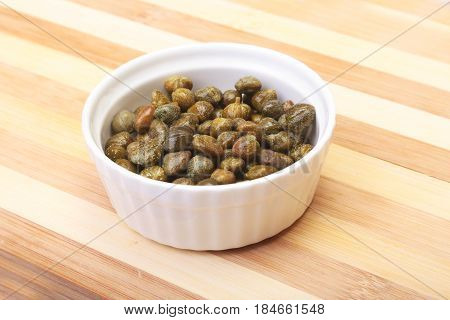 bowl with fresh capers on wooden table.