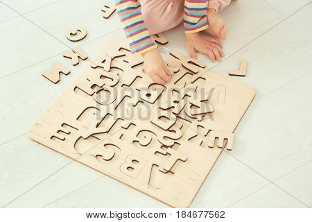 Cute little child playing with letters while sitting on floor at home