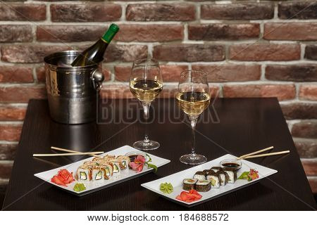 Two sets of sushi rolls on white plate with chopsticks and wine glasses