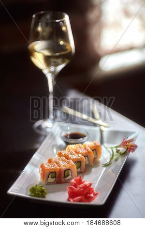 Philadelphia maki sushi rolls with salmon cheese cream cucumber on white plate and glass of wine