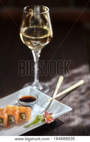 Philadelphia maki sushi rolls with salmon cheese cream cucumber on white plate and glass of wine