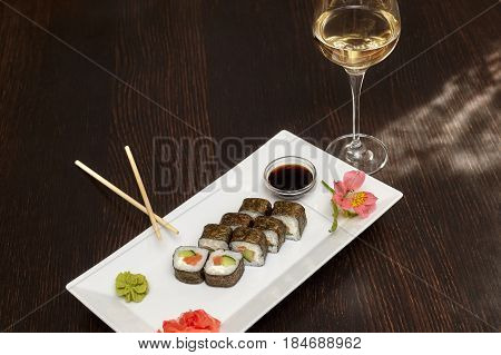 Sushi rolls with salmon and nori on white plate and glass of wine