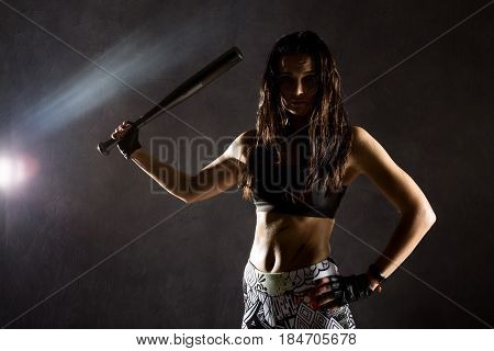 sexy athletic woman with baseball bat on dark background in the beam of a searchlight.