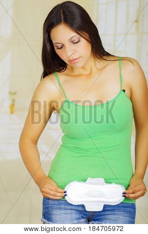 Young beautiful woman with a green blouse holding a hygenic towel, pointing in front of her body.