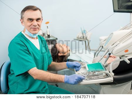 Portrait Of Handsome Male Dentist With Dental Devices In The Dental Clinic. Doctor Wearing Mask, Gre