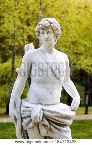 Sculpture in classic style. Statue of a man hunter with bow in the park.