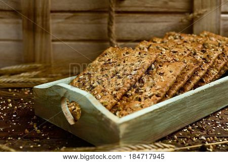 closeup of some appetizing brown crackers topped with different seeds a green pale wooden tray placed on a wooden table