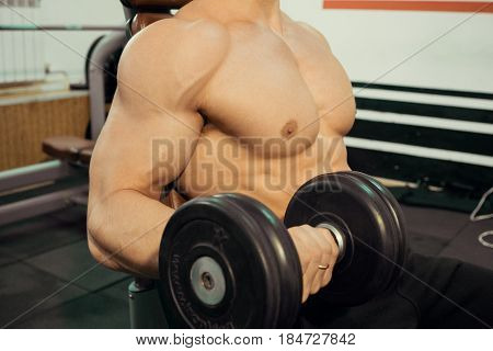 Bodybuilder with a press swinging biceps in the gym