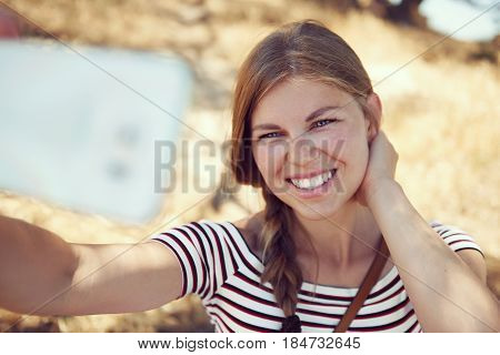 Pretty smiling woman taking picture of herself over rural background outdoors. Concept of summer holidays and travel.