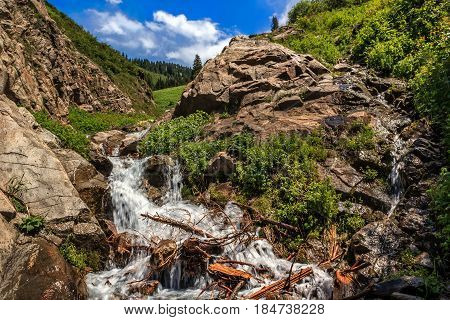 Waterfall in the rocks against the backdrop of mountains and sky with clouds