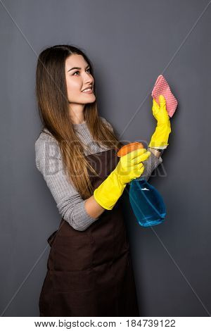 Young Woman Use Spray While Cleaning Up House Posing For Camera On Grey Background