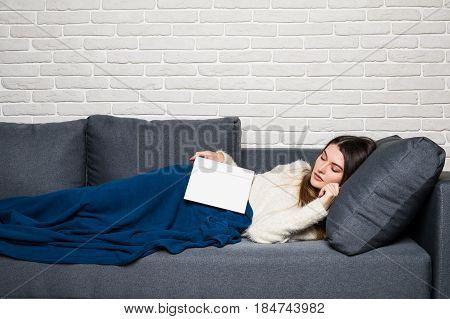 Tired Young Woman Taking A Nap At Home Lying On A Sofa With A Book Lying Across Her Chest And Her Ey