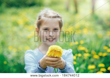 beautiful blue-eyed and blond girl in a meadow holding a dandelion in the hands