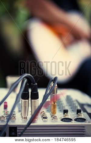 Cables connected to audio amplifier and an unrecognizable guitarist in the back. Shallow depth of field