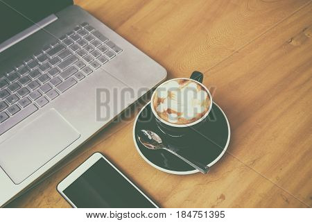 Laptop computer with smarth phone on wooden desk in business room. A cup of coffee in coffee break time (Film grain effect)