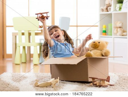 Kid girl playing pilot flying a cardboard box in children room