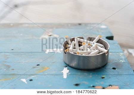 Various cigarette butts in dirty full ashtray