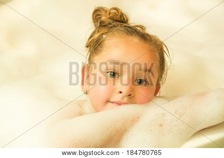 little beautiful girl posing inside of a bathtub with water and foam in bath.
