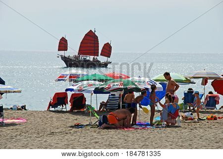 TORREMOLINOS, SPAIN - SEPTEMBER 3, 2008 - Tourists relaxing on the beach with a junk ship out to sea Torremolinos Malaga Province Andalusia Spain Western Europe, September 3, 2008.