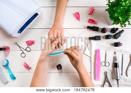 Manicure for the client. Close-up of the hands of a manicurist and client on a wooden background. Nail care. Manicure set and nail polish.