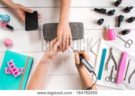 Manicure for the client. Close-up of the hands of a manicurist and client on a wooden background. Nail care. Manicure set and nail polish.