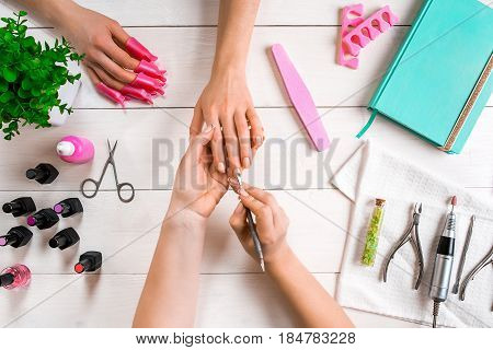 Manicure for the client. Close-up of the hands of a manicurist and client on a wooden background. Nail care. Manicure set and nail polish.