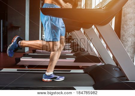 Legs running on the treadmill close up. A muscular man in yellow sneakers and blue shorts running down the treadmill in the gym. Motion blur