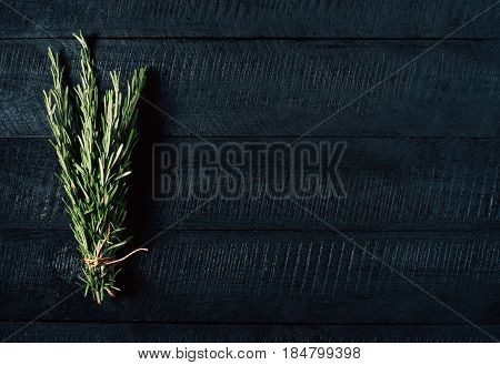 Green rosemary bunch on black vintage wooden background close up top view natural organic aromatic food on kitchen table vegan spice on mock up seasoning herb on cooking process copy space