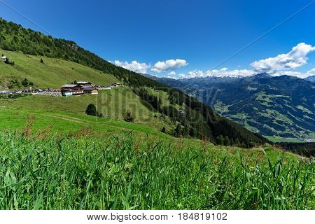 Low angle view of green meadow and alpine village with high mountains under blue sky. Austria Tirol Zillertal Zillertal High Alpine Road