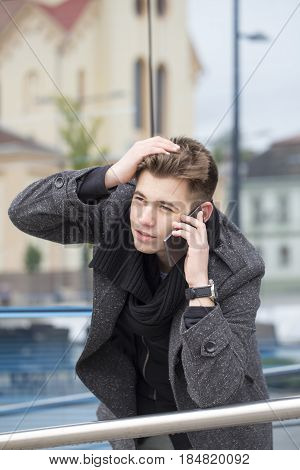 Handsome attractive young man in coat holding a mobile phone in hand and talking