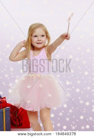 Adorable little Princess with a magic wand in the hands is surrounded by a beautifully Packed boxes with gifts. In the Christmas holiday. A girl waves a magic wand , she casts a magic spell.