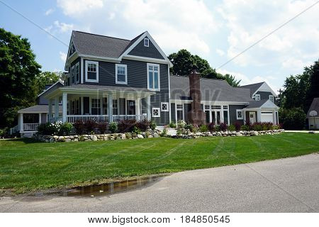 A large, elegant home, with a wraparound porch and an attached garage, on Fourth Street in Harbor Springs, Michigan, during August.