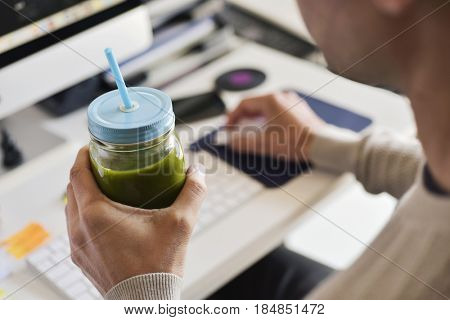 closeup of a young caucasian man drinking a green detox smoothie served in a glass jar at the office